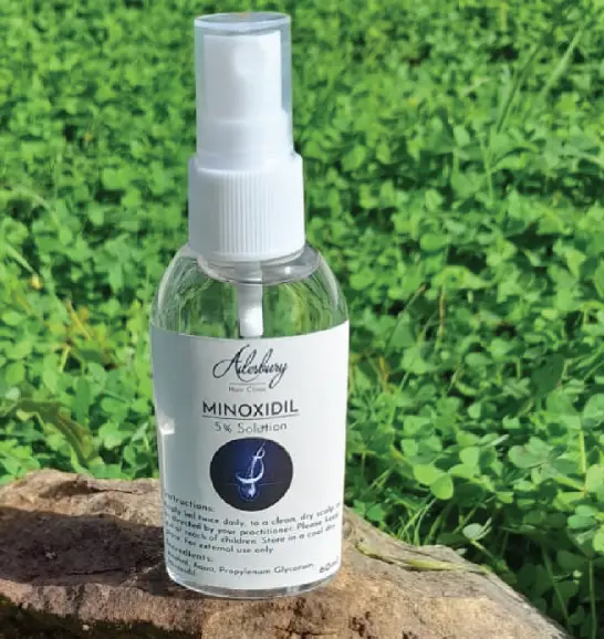 a bottle of minoxidil treatment for hair loss laying on top of a rock